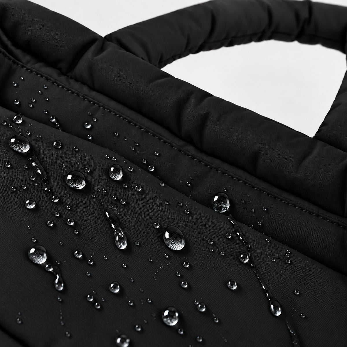 Water droplets beading on the black PUFFER Mini tote bag, showing its water-repellent fabric designed to help protect against light rain.