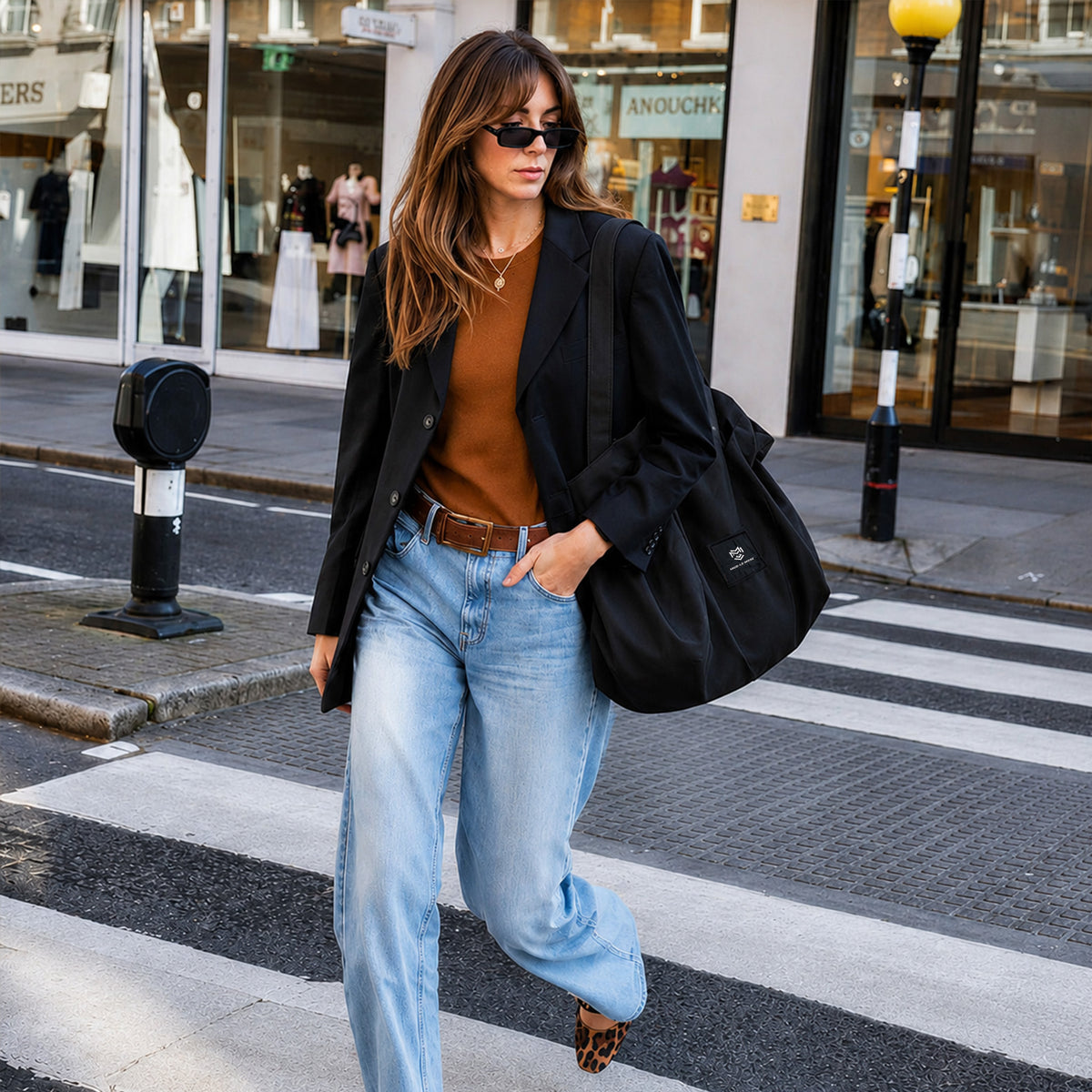woman carrying the mod le mode oyster black lay-flat tote bag while walking across a city street in a casual smart outfit